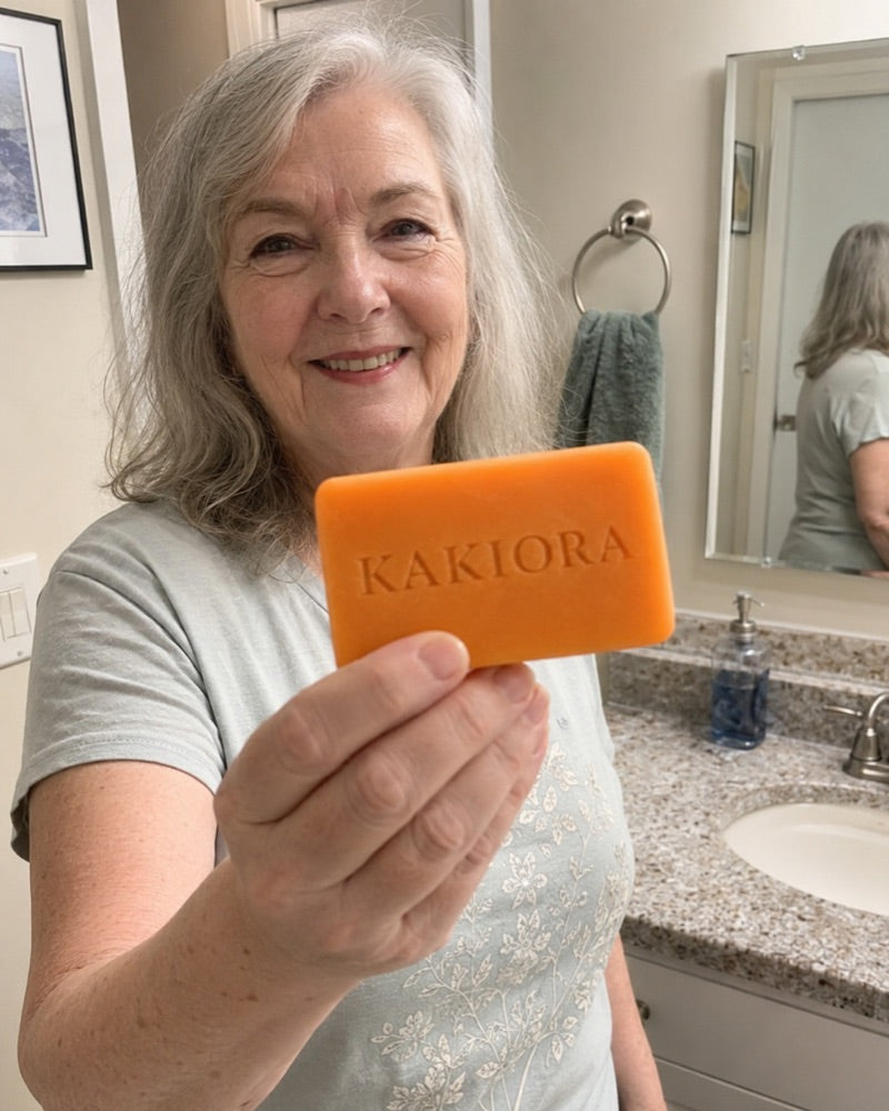 Older woman in her bathroom holding out a bar of KAKIORA persimmon soap