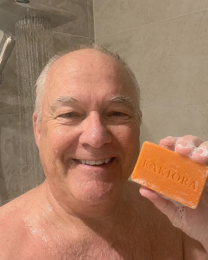 Older man in the shower washing with a lathered bar of KAKIORA persimmon soap